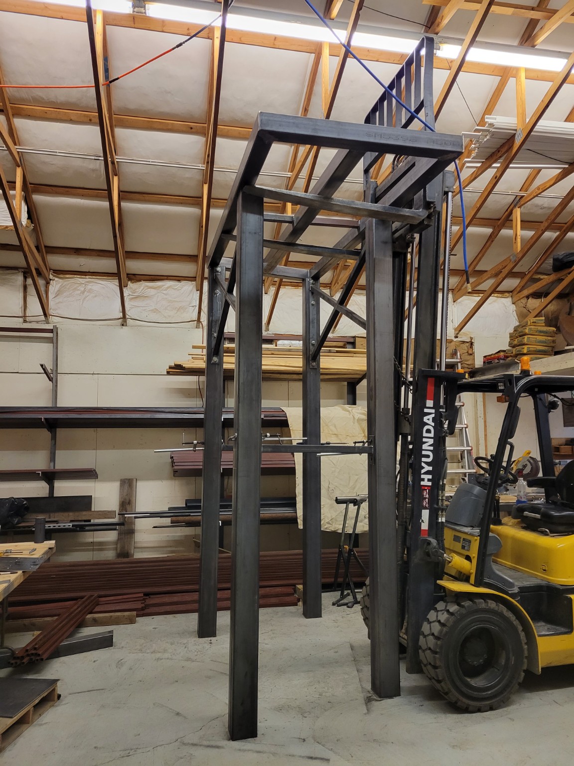 A forklift lifting and positioning a large custom fabricated steel frame in the shop