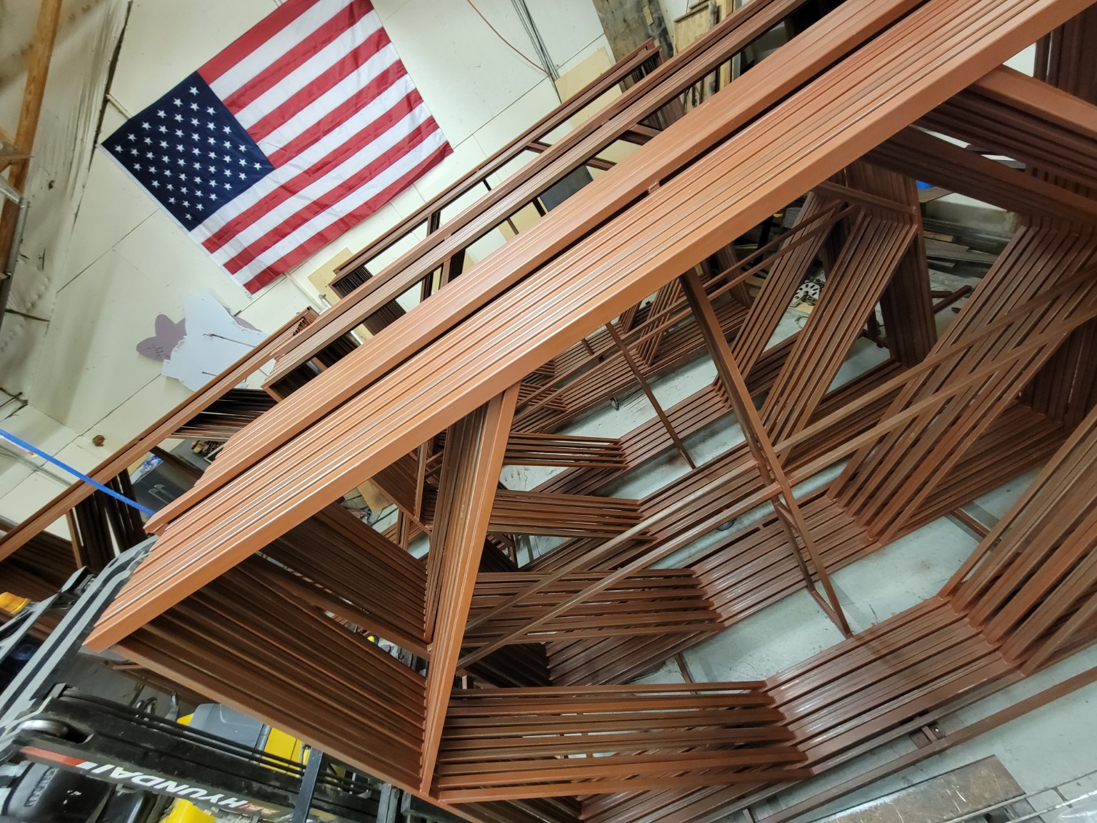 Completed welded steel frames stacked in the fabrication shop beneath an American flag